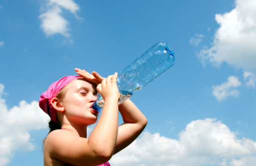 A woman carrying an exercise mat on her back, holding a bottle of water and smiling. Tired after exhausting workout