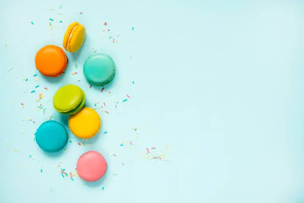 Photo of Colorful macaroons and sugar sprinkles arranged over blue background. Copy space.