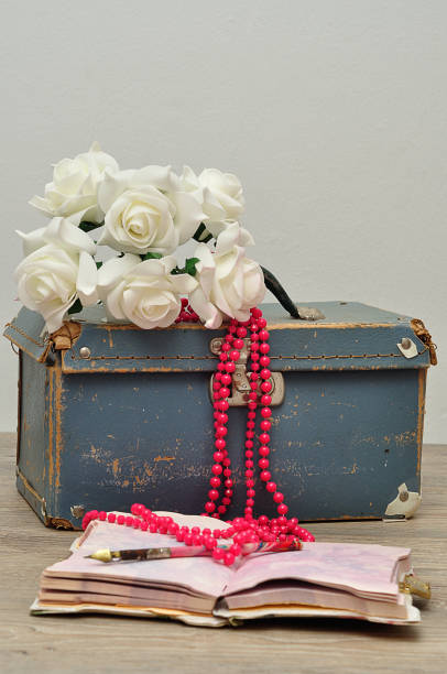 istock An old worn out blue suitcase with a bunch of artificial white roses, a string pink beads, a note book and a pen 928768992