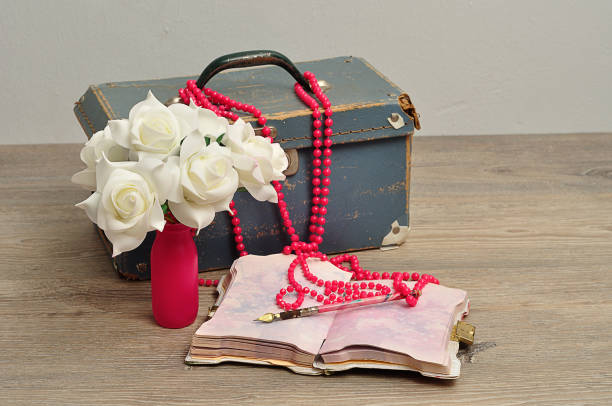 istock An old worn out blue suitcase with a bunch of artificial white roses, a string pink beads, a note book and a pen 928769026