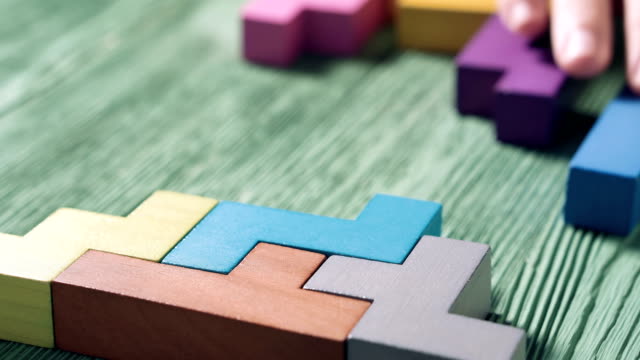 Close up of man's hand folding colorful wooden blocks on the green table background. The concept of logical thinking.