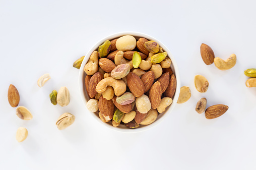 Healthy food and snack : mixed nuts in white ceramic bowl on white background from above, pistachios, almonds, hazelnuts and cashew