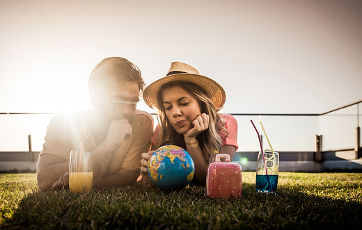 Thoughtful couple relaxing on a penthouse patio and choosing their next travel destination on a globe.