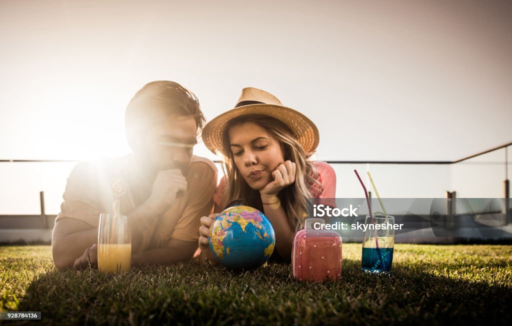 Hmm, where should we go on our vacation? Thoughtful couple relaxing on a penthouse patio and choosing their next travel destination on a globe. Vacations Stock Photo