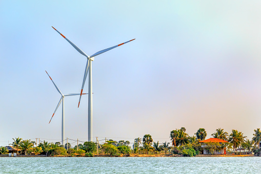 Wind generators in a jungle on a lake near a small fishing village on a sunny day against a blue sky with clouds