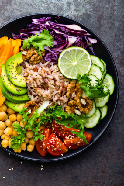 istock Buddha bowl dish with brown rice, avocado, pepper, tomato, cucumber, red cabbage, chickpea, fresh lettuce salad and walnuts. Healthy vegetarian eating, super food. Top view 928811688