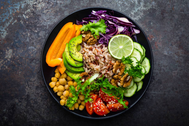 istock Buddha bowl dish with brown rice, avocado, pepper, tomato, cucumber, red cabbage, chickpea, fresh lettuce salad and walnuts. Healthy vegetarian eating, super food. Top view 928820086