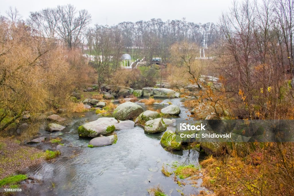 View from the bridge on a small river that flows through the boulders and the granite stone  canyon in the background on the hillside park with pavilions and stairways. Autumn and rainy weather Autumn Stock Photo