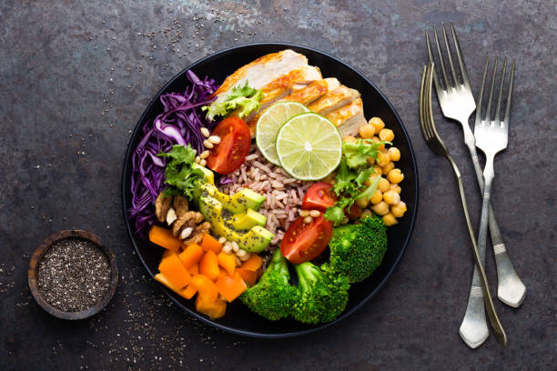istock Buddha bowl dish with chicken fillet, brown rice, avocado, pepper, tomato, broccoli, red cabbage, chickpea, fresh lettuce salad, pine nuts and walnuts. Healthy balanced eating. Top view 928822520