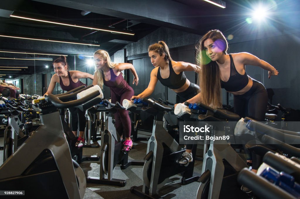 Group of fitness girls riding exercise bikes together on cycling class at gym. Stationary Cycling Class Stock Photo