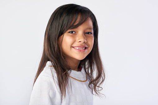 Caucasian little girl wearing white t-shirt is looking at camera with a cute smile in front of white background.