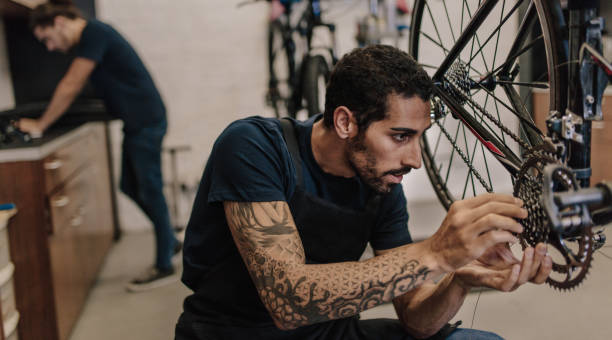 Mechanic repairing a bicycle in workshop Man fixing a bicycle in a repair shop. Worker fixing bicycle gear and chain in workshop. bike workshop stock pictures, royalty-free photos & images