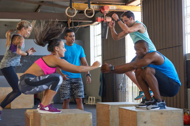 Instructor giving encouragement while fit strong healthy people do box jumps Instructor giving encouragement while fit strong healthy people do box jumps in cross training gym fitness boot camp stock pictures, royalty-free photos & images