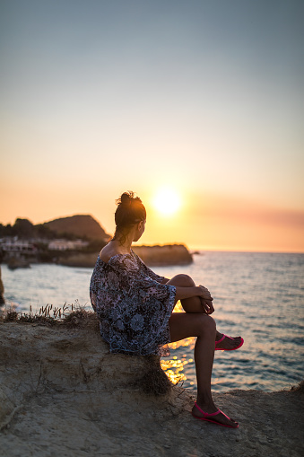 Pretty Woman Sitting On Pier And Looking At Sunset On Sea Horizon