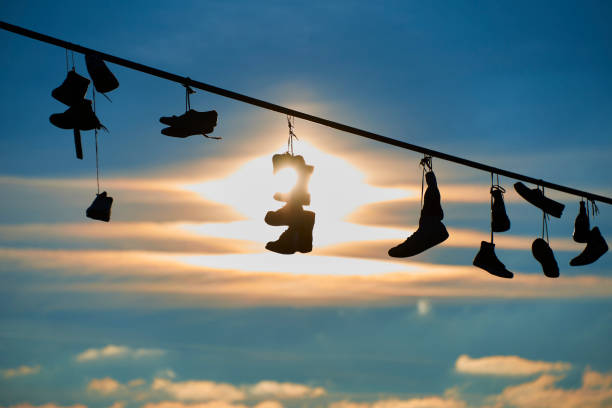 istock Old Shoes hanging on electrical wire against a sky 928856118