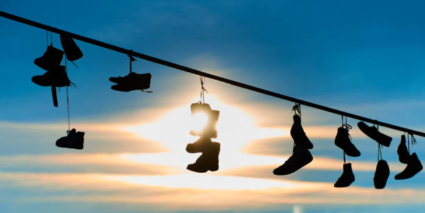 istock Old Shoes hanging on electrical wire against a sky 928856124