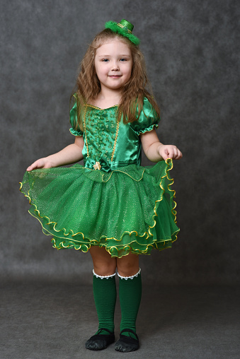 Little girl with long ginger hair in green emerald carnival costume and leprechaun glitter mini top hat