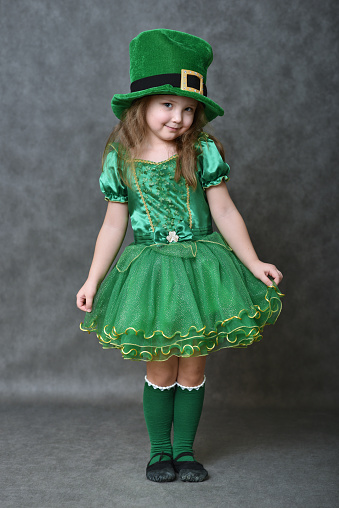 Little girl in green emerald costume and leprechaun top hat on dark grey background