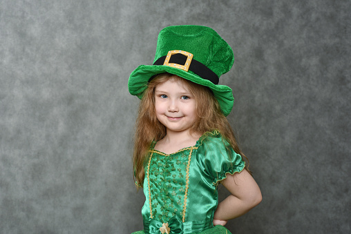 Little girl in green emerald dress and leprechaun top hat with golden buckle looking at camera