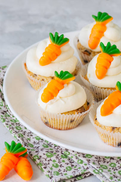 istock Vanilla cupcakes with chocolate chips and cream cheese frosting decorated with carrot marmalade in a plate on a white stone background. 928865924