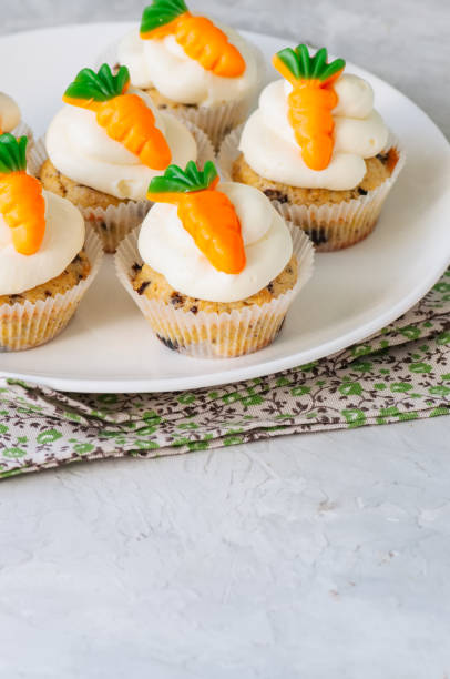 istock Vanilla cupcakes with chocolate chips and cream cheese frosting decorated with carrot marmalade in a plate on a white stone background. 928865936