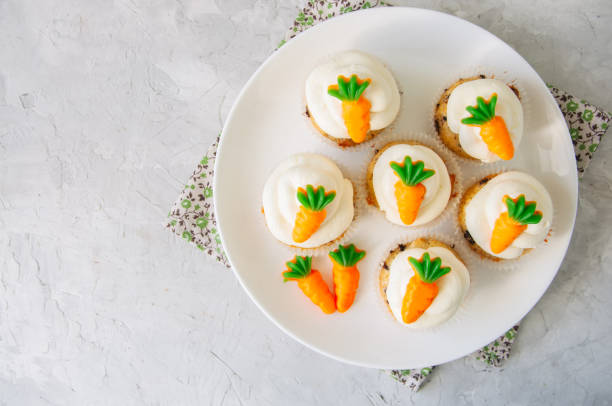 istock Vanilla cupcakes with chocolate chips and cream cheese frosting decorated with carrot marmalade in a plate on a white stone background. 928865946