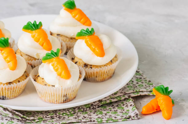 istock Vanilla cupcakes with chocolate chips and cream cheese frosting decorated with carrot marmalade in a plate on a white stone background. 928865952