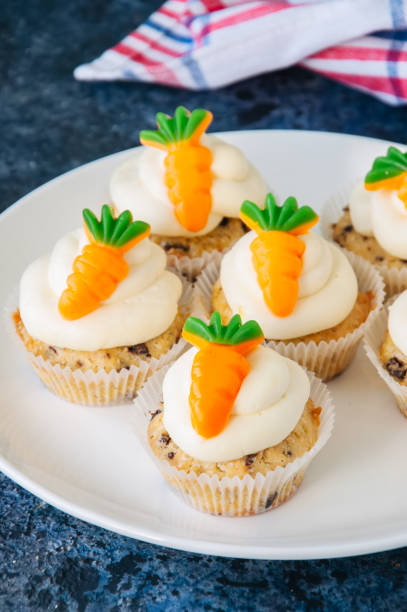 istock Vanilla cupcakes with chocolate chips and cream cheese frosting decorated with carrot marmalade in a plate on a blue stone background. 928866032