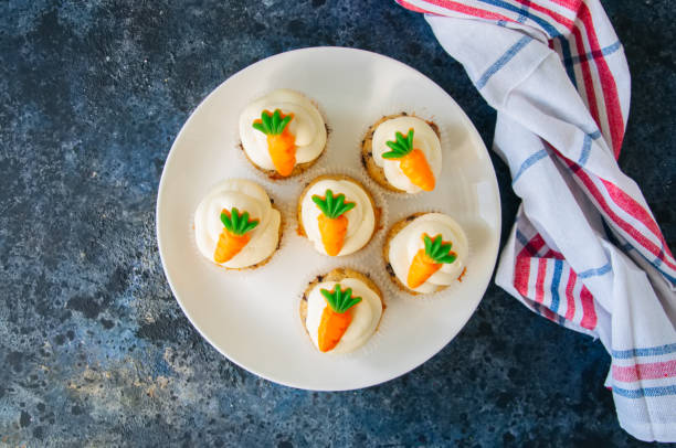 istock Vanilla cupcakes with chocolate chips and cream cheese frosting decorated with carrot marmalade in a plate on a blue stone background. 928866036