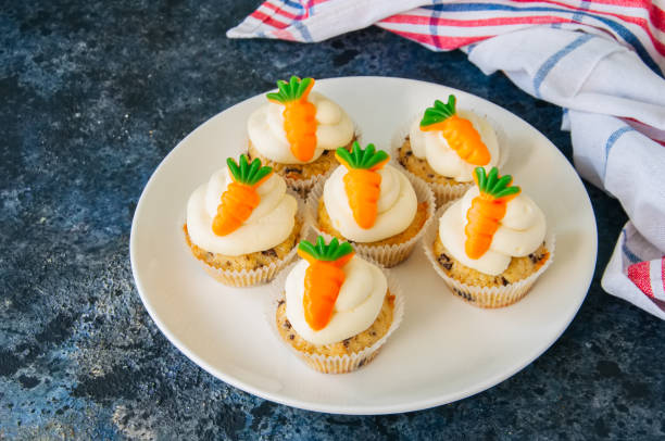 istock Vanilla cupcakes with chocolate chips and cream cheese frosting decorated with carrot marmalade in a plate on a blue stone background. 928866054