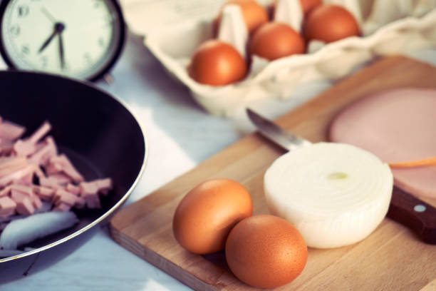 Hasty preparation of a breakfast of fried eggs with sausage and onions in the morning before leaving for work