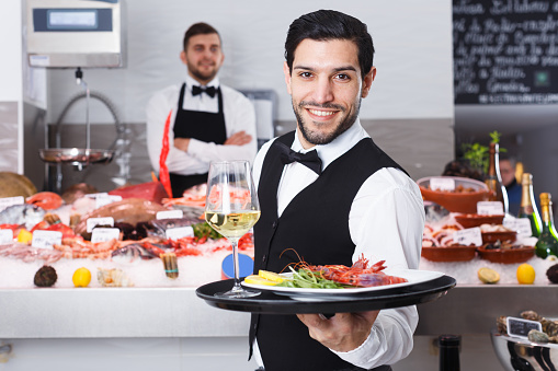 Portrait of smiling waiter with serving tray offering dishes in fish restaurant