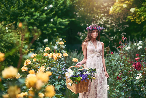 Shot of a beautiful young woman wearing a floral head wreath and holding a basket full of flowers in nature