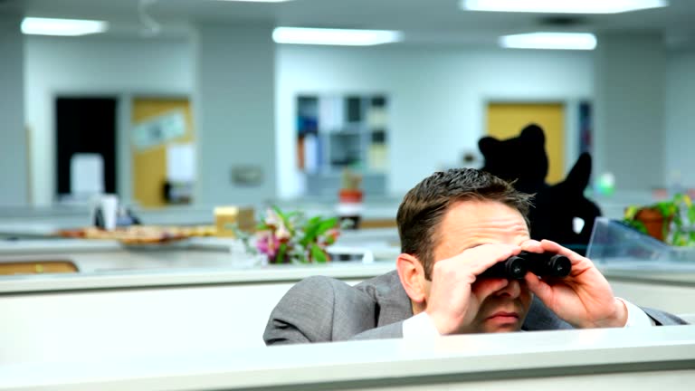 Businessman peeking over cubicle with binoculars