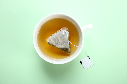 Mint tea bag in a cup on a mint pastel background. Top view.