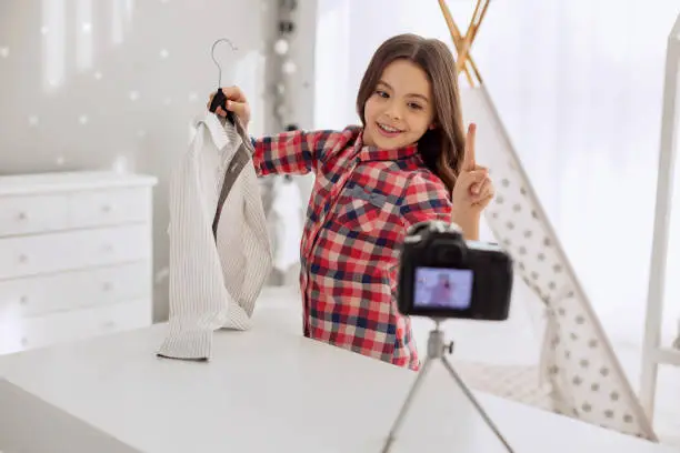 It is bargain. Joyful pre-teen girl holding a new shirt and making remarks about its quality and price while recording a video blog
