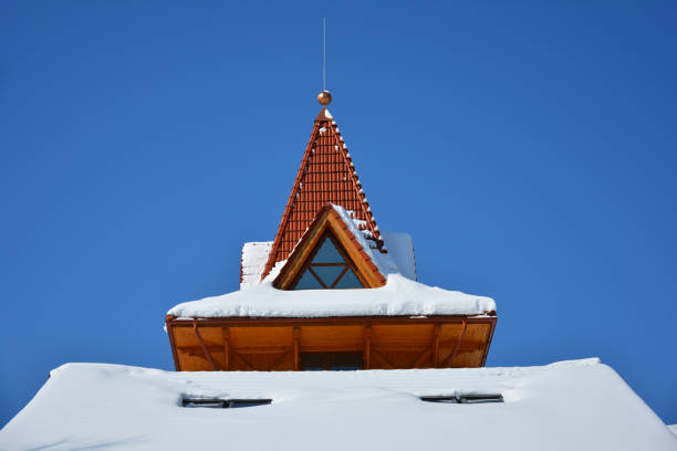 istock Attic window of triangular shape on snow-covered roof on background of bright blue sky. Sunny winter day. 928891782
