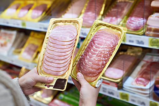 Woman chooses a slice of ham and meat  in vacuum package at the grocery store