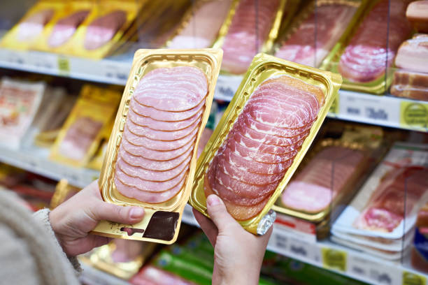 Woman chooses slice of ham at store Woman chooses a slice of ham and meat  in vacuum package at the grocery store delicatessen stock pictures, royalty-free photos & images