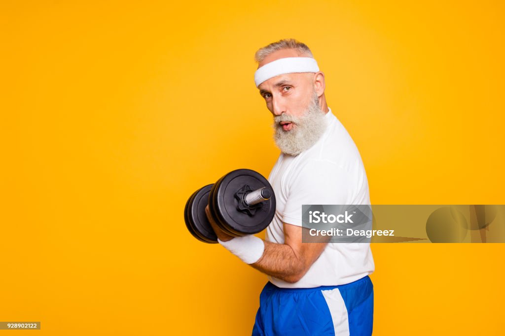 Cool playful flirty naughty strong grandpa with confident grimace exercising holding equipment up, lifts it with strength and power. Body care, fitness, body building, hobby, weight loss lifestyle Senior Adult Stock Photo