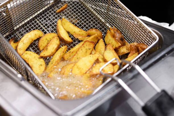 Spicy potato chips or wedges in a deep fryer Spicy potato chips or wedges cooking in a deep fryer in a close up view of the hot bubbling oil and wire metal basket deep fryer stock pictures, royalty-free photos & images