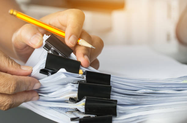 istock Businessman hands searching and checking write unfinished documents stacks of paper files on office desk for report papers with pencil, piles of sheet achieves clips, Document is written presented. 928906550