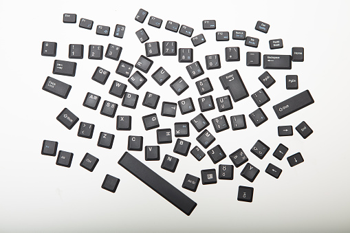 Loose alphanumeric covers for the keys on a computer keyboard in a random jumble on a white or light silver background viewed from overhead centered in the screen with surrounding copy space