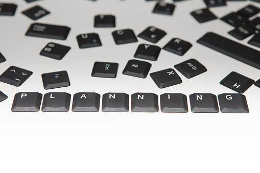 Loose scattered alphanumeric and function key covers from a laptop computer keyboard with the word Planning and digits in a close up high angle conceptual view