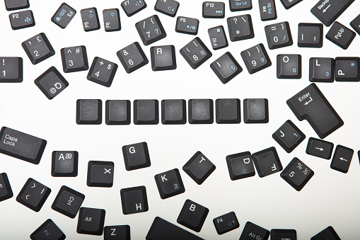 Loose scattered alphanumeric and function key covers from a laptop computer keyboard with a line of blank keys viewed from above