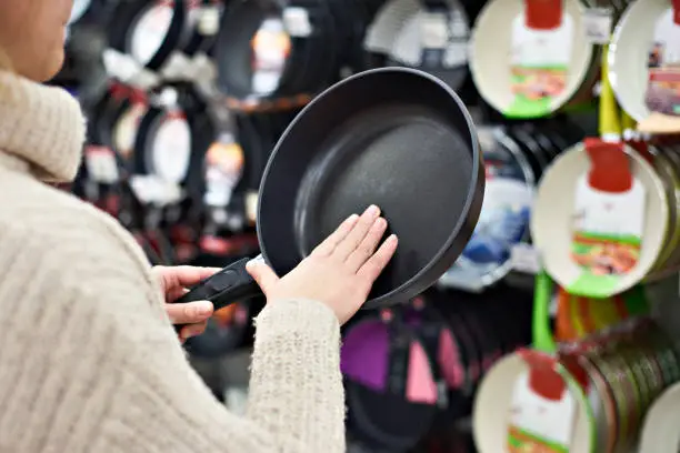 Photo of Woman chooses frying pan in crockery store