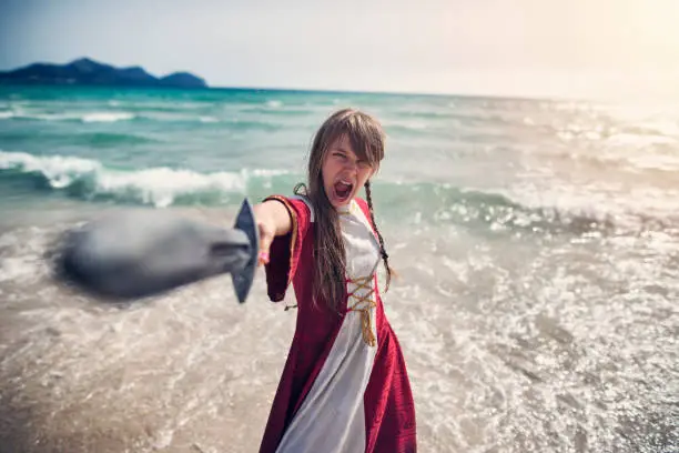 Young viking shieldmaiden practicing with sword on the beach. 
