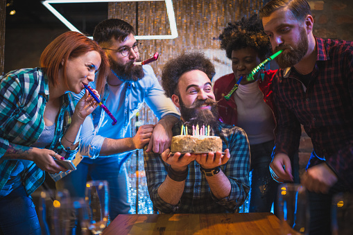 Group Of Friends celebrating birthday. Bearded man blowing out  birthday cake candles