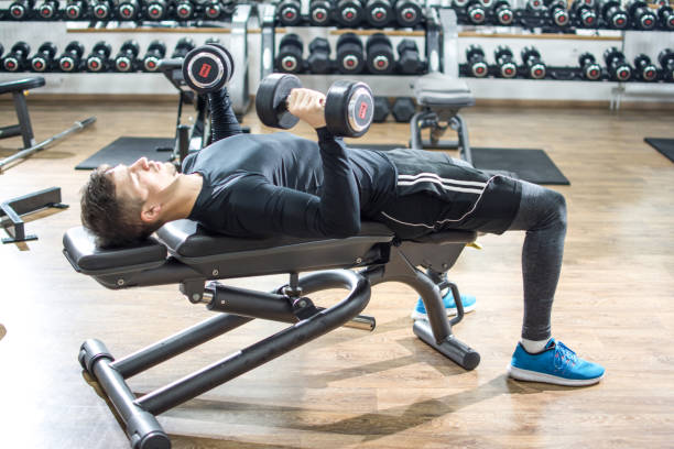 istock Handsome young man lying on exercise bench and lifting dumbbells at gym. 928995044
