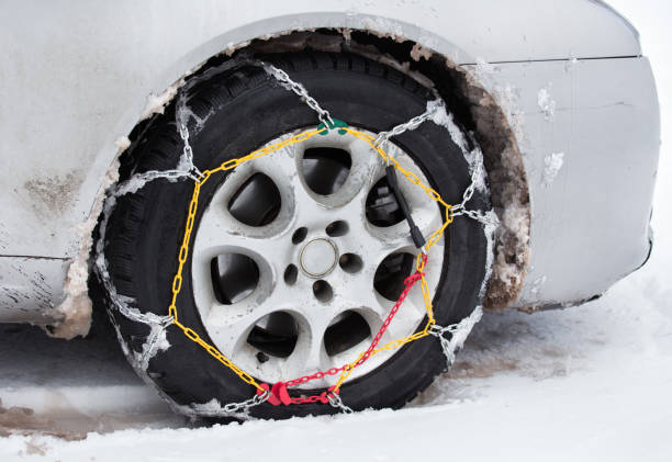 Front view of tire chains on car wheel on dirty vehicle in snow